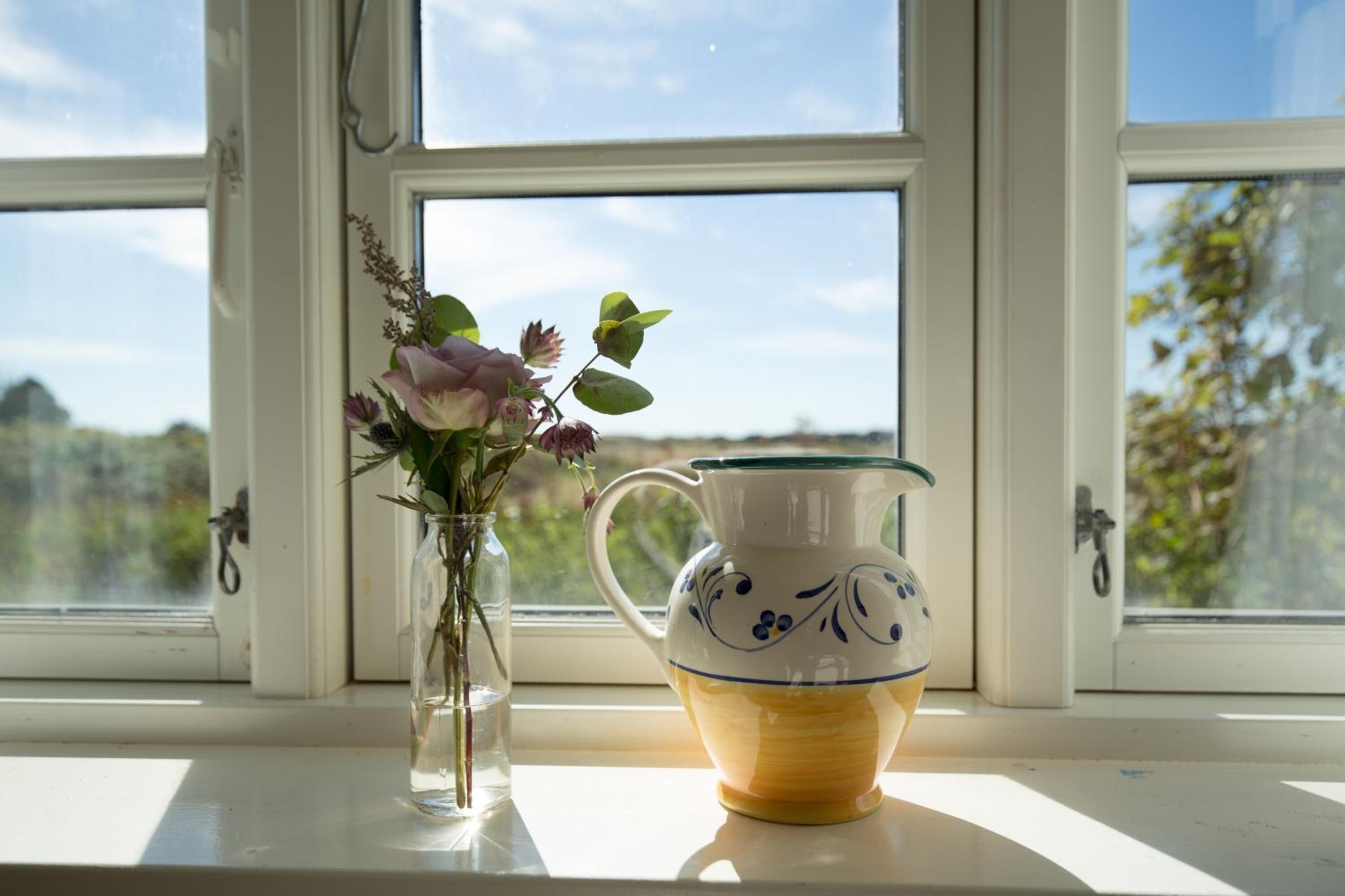 A window with a vase of flowers and a pitcher on the windowsill.