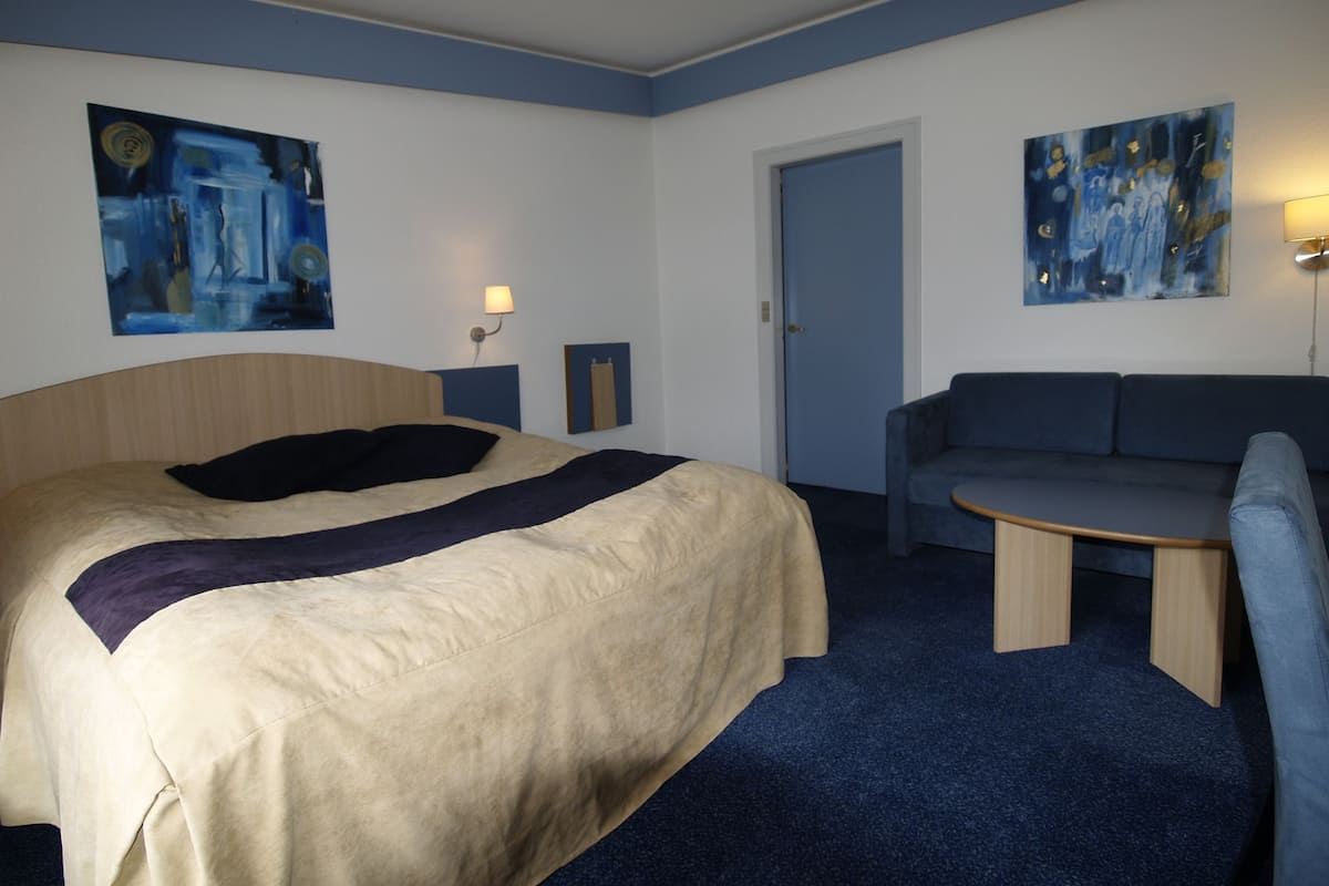 Une chambre d’hôtel avec un lit, un canapé, une petite table et deux tableaux accrochés aux murs.