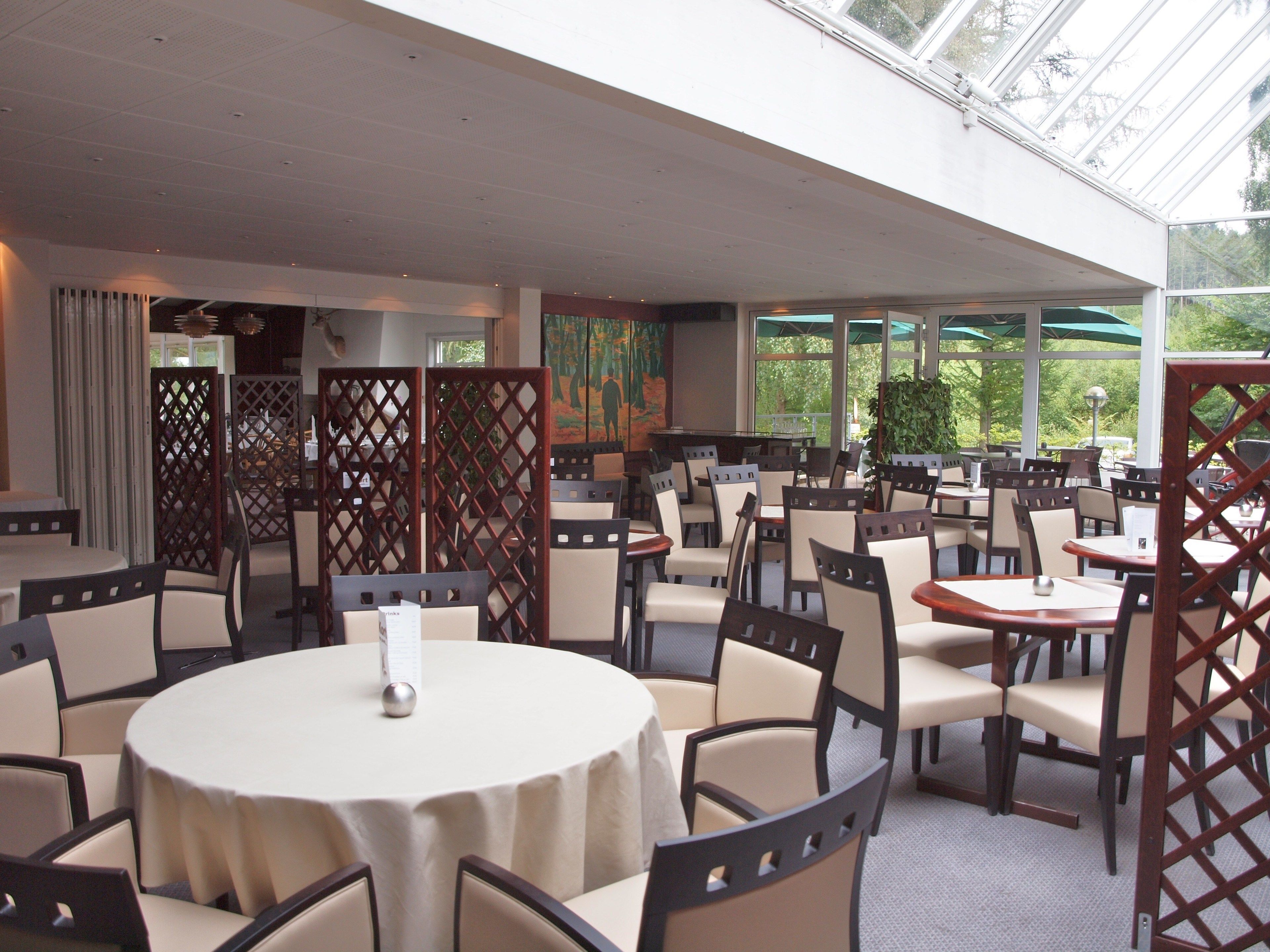A restaurant with round tables and chairs, a high ceiling, and large windows.