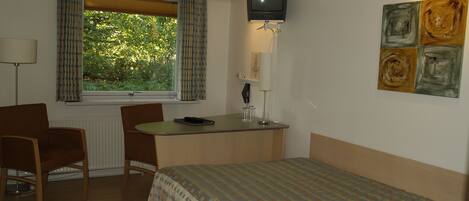 Habitación de hotel con cama, escritorio, dos sillas, televisor y ventana con cortinas.