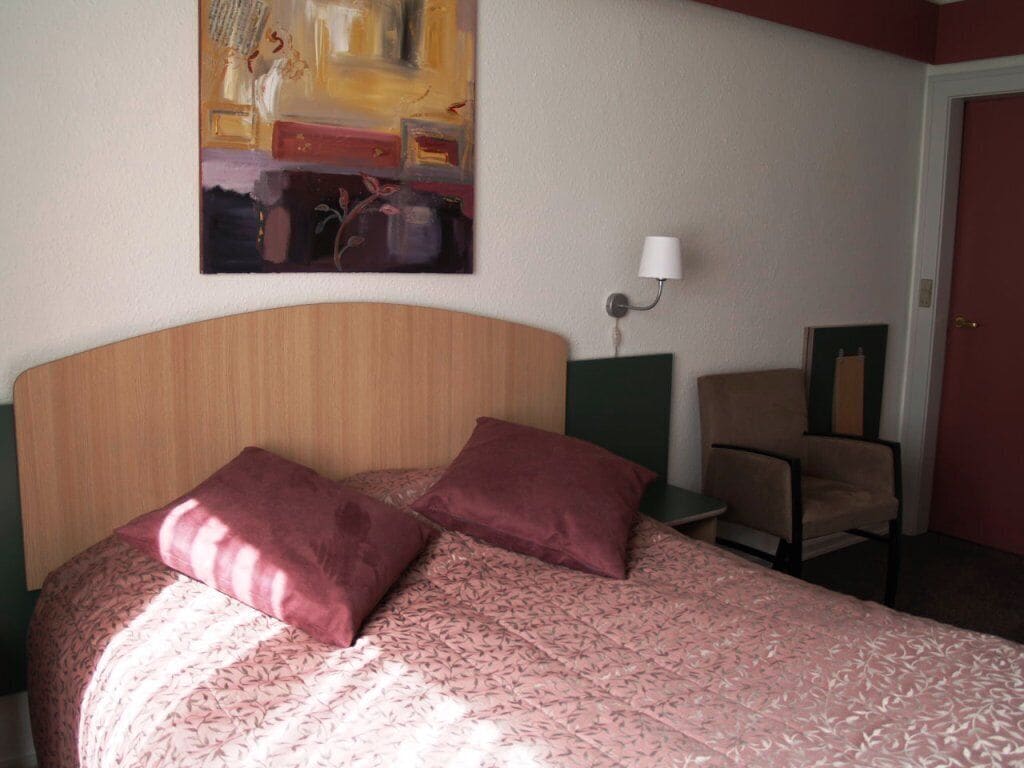 Une chambre d’hôtel avec un lit, un tableau au mur, une chaise et une lampe.