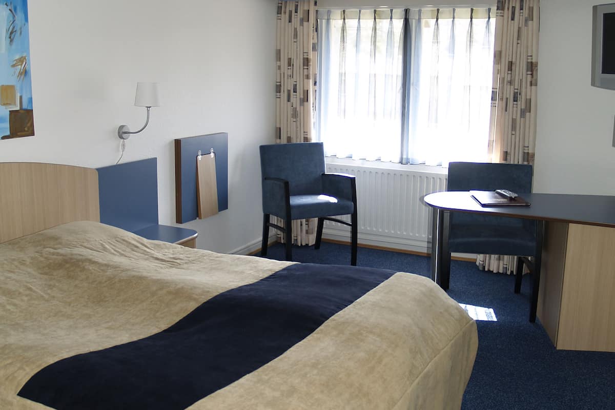 Une chambre d’hôtel avec un lit, un bureau, une chaise et une fenêtre avec des rideaux.