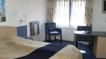 A hotel room with a bed, a desk, a chair, and a window with curtains.