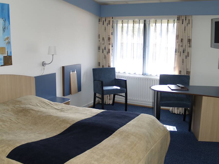 A hotel room with a bed, a desk, a chair, and a window with curtains.