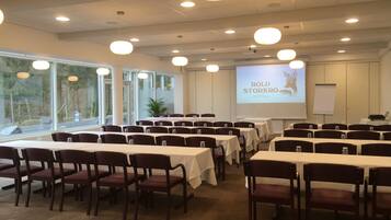 Ein Konferenzraum mit Tischen, Stühlen, großen Fenstern und einer Präsentationsleinwand.