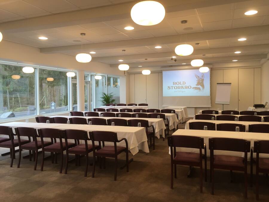 A conference room with tables and chairs, large windows, and a presentation screen.