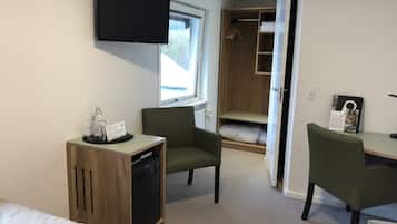 Una habitación de hotel compacta con cama, escritorio, silla, televisor y armario.