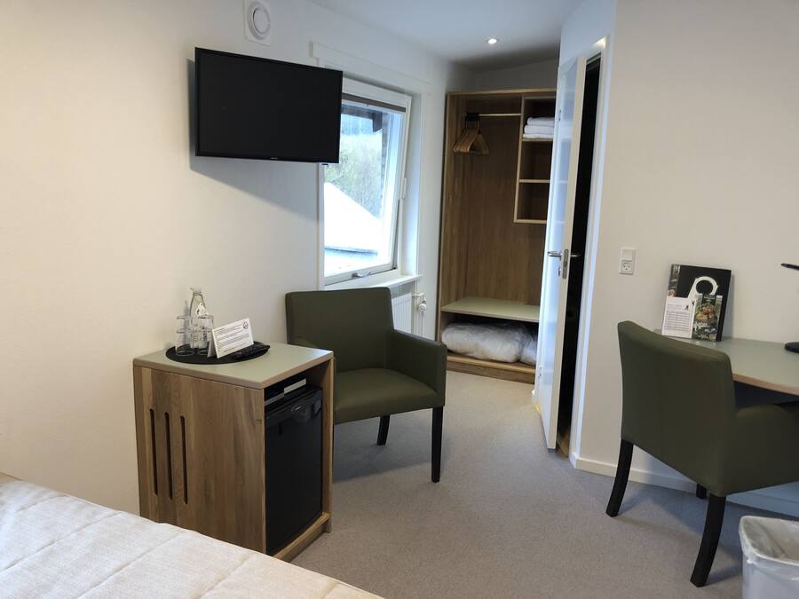 Una habitación de hotel compacta con cama, escritorio, silla, televisor y armario.
