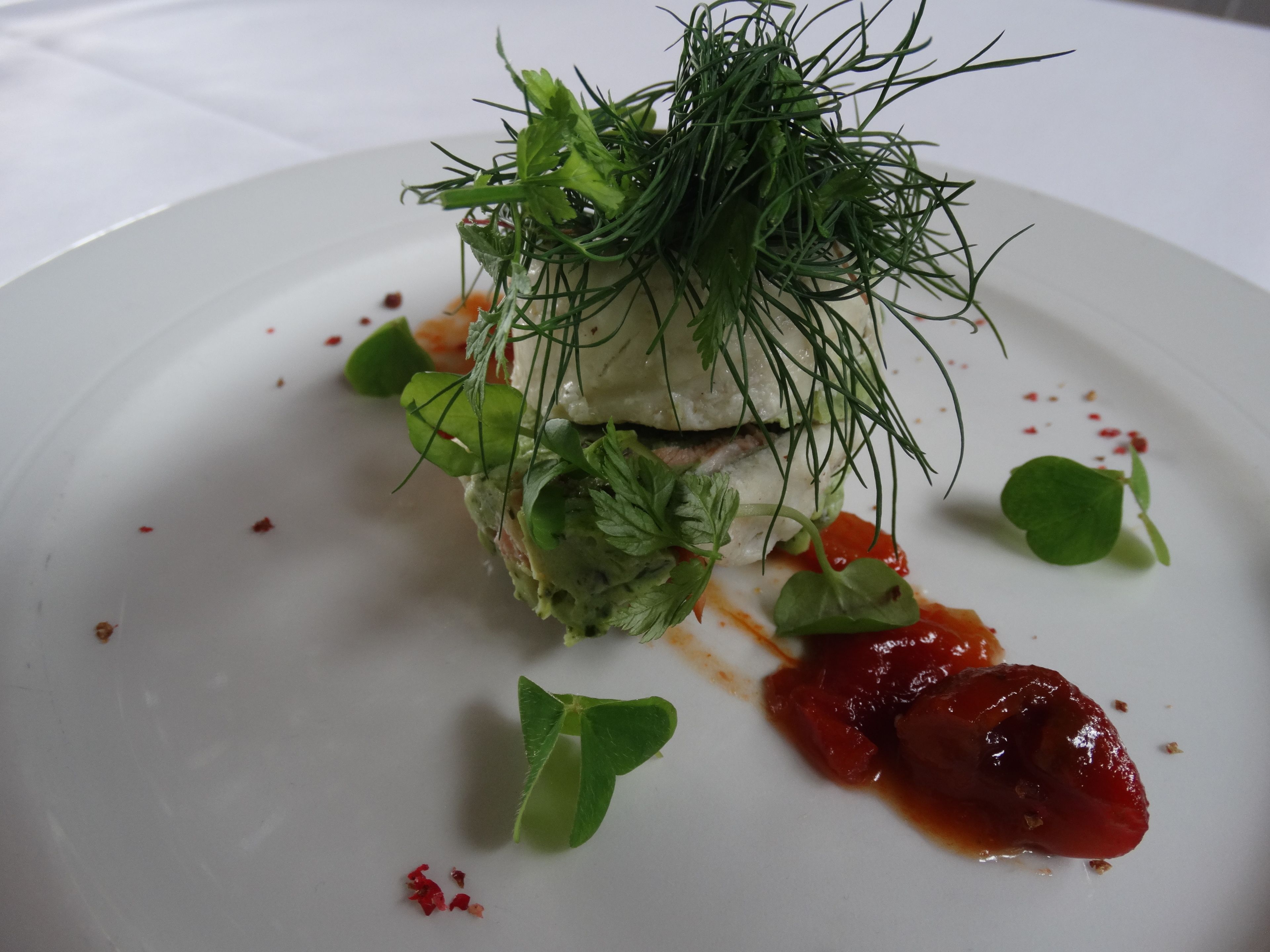 A white plate with a food dish garnished with green leaves and sauce.