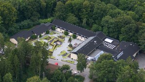 En vy över ett hotell med en innergård, omgivet av tät skog, sedd från luften.