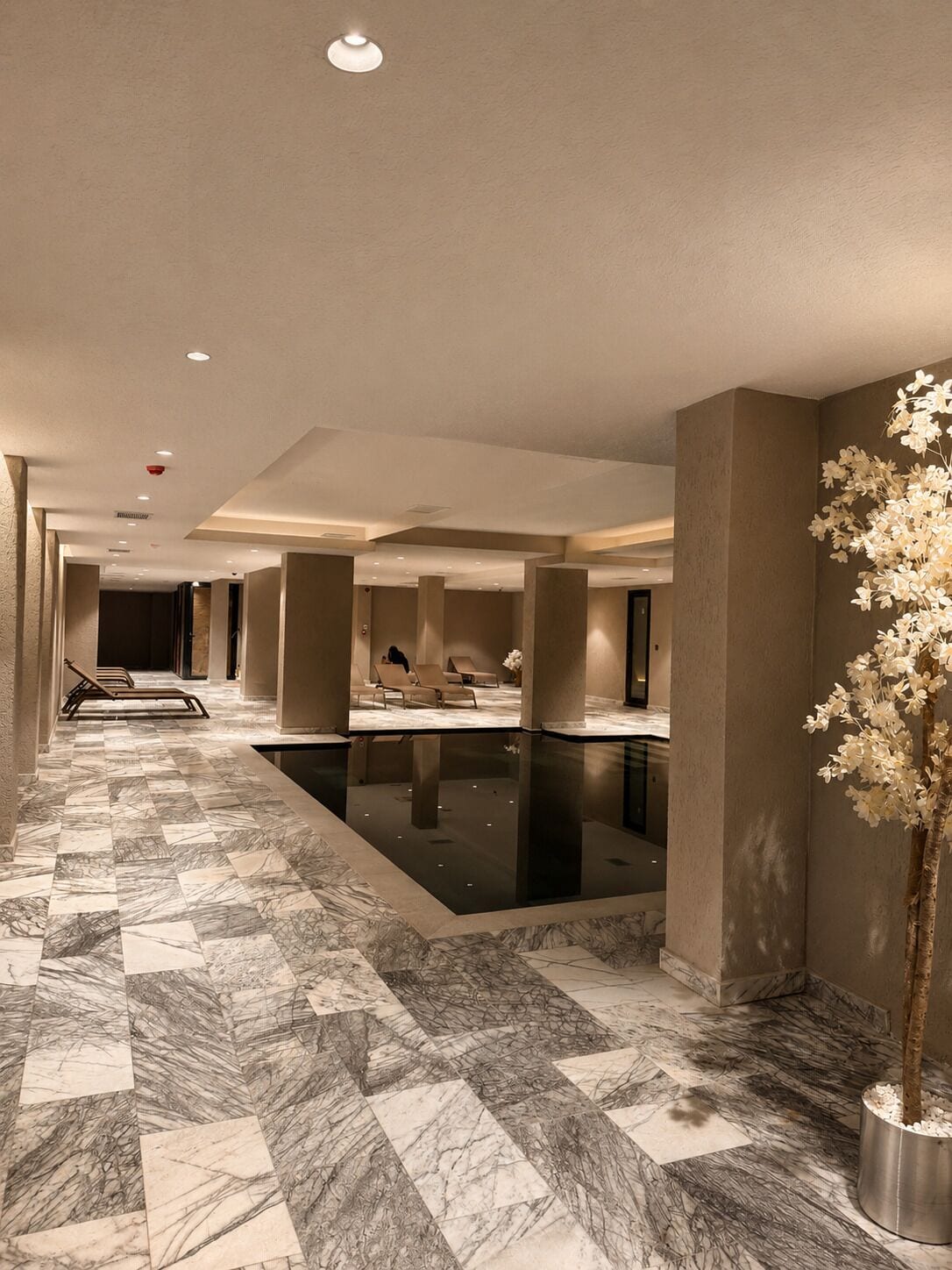 Een hotel lobby met een marmeren vloer, een zwembad en lounge stoelen.