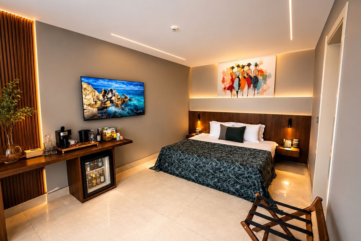 Una habitación de hotel moderna con cama, mesitas de noche, televisor, obras de arte y minibar.