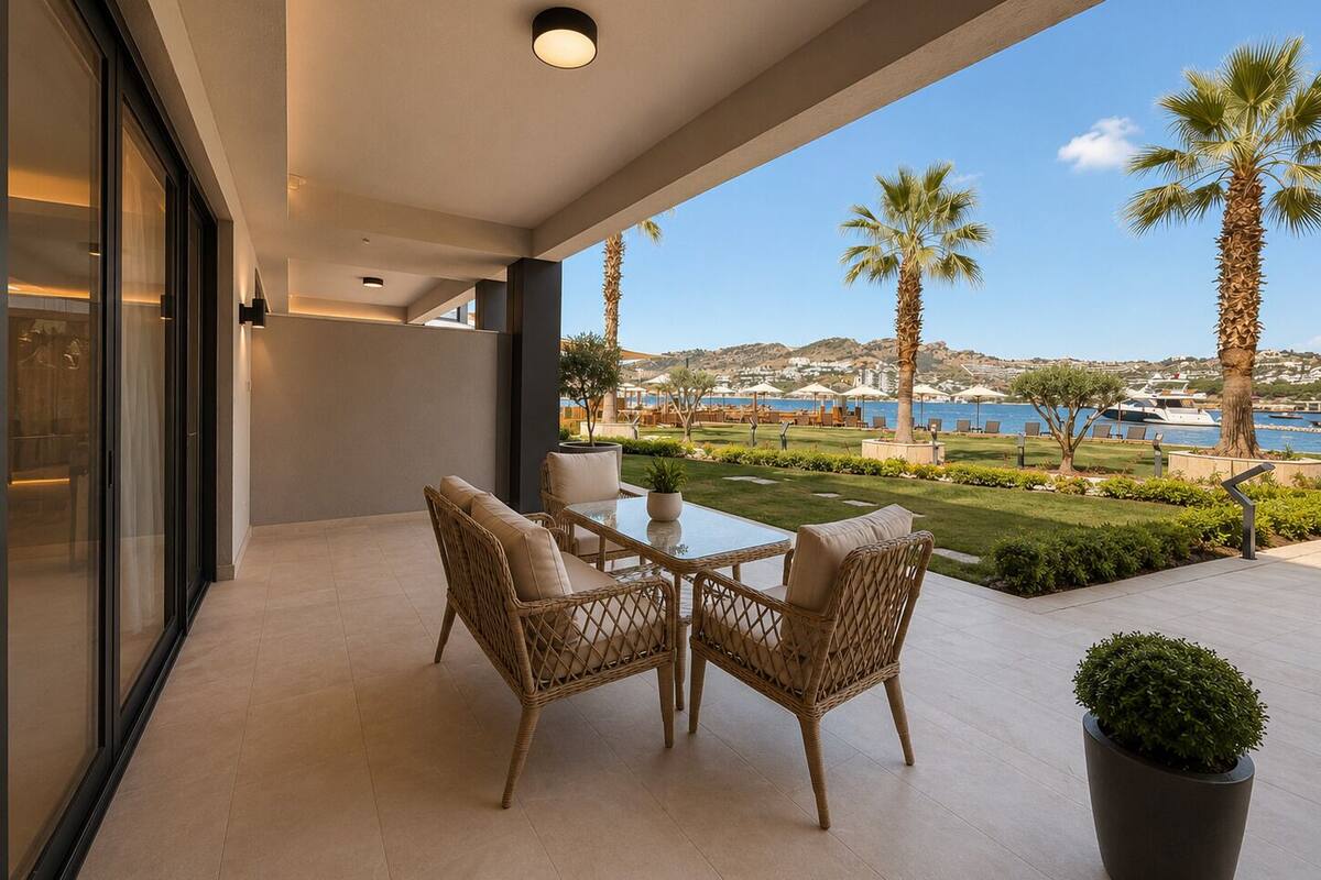 Eine Terrasse im Freien mit Korbmöbeln, Blick auf das Meer und Palmen.