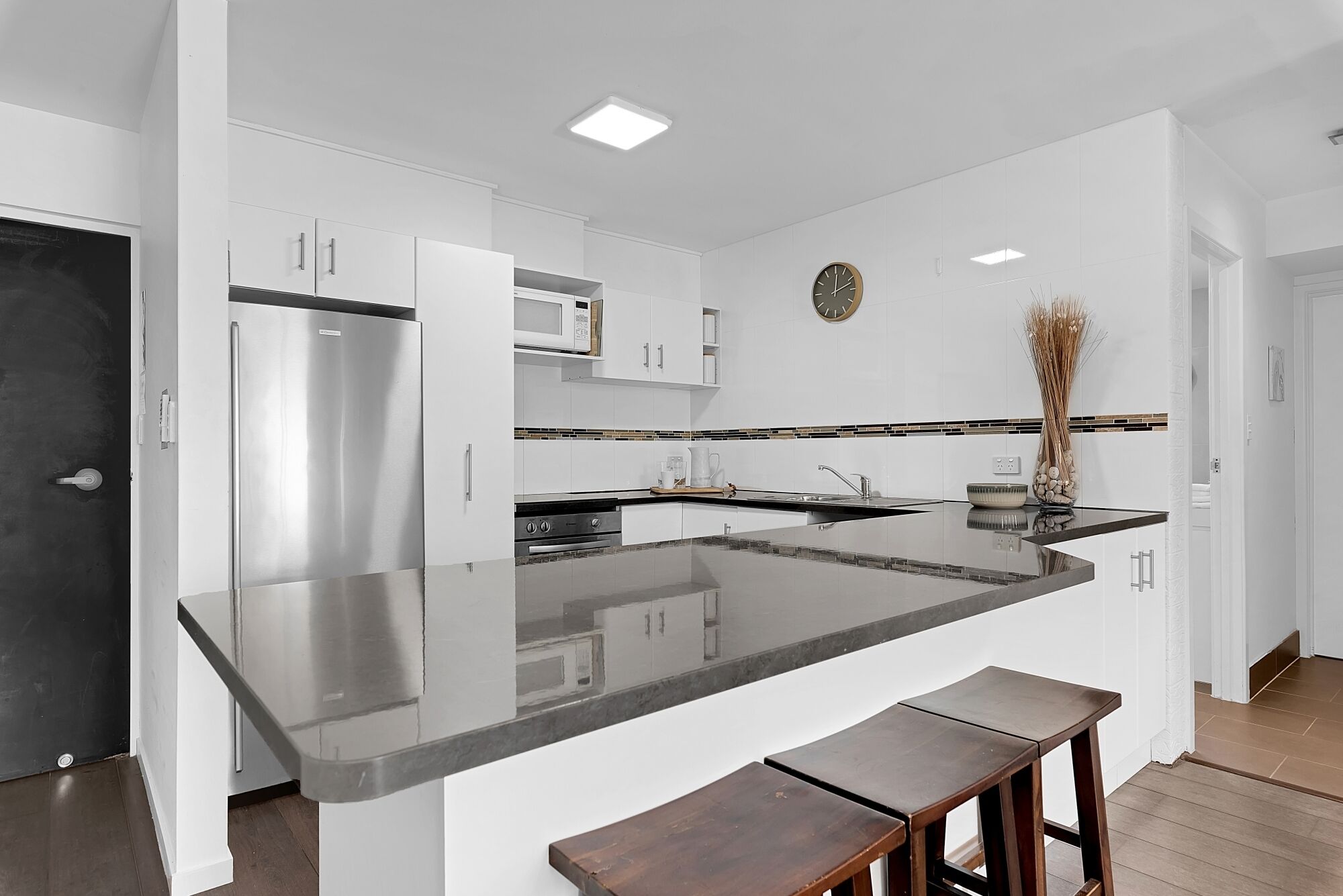 Una cocina moderna con muebles blancos, un refrigerador de acero inoxidable, un microondas y una isla grande con taburetes de bar.