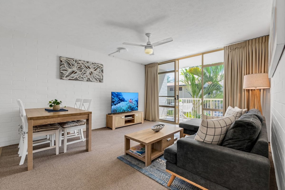 A modern living room with a sofa, a coffee table, a TV, and a dining area with a table and chairs.