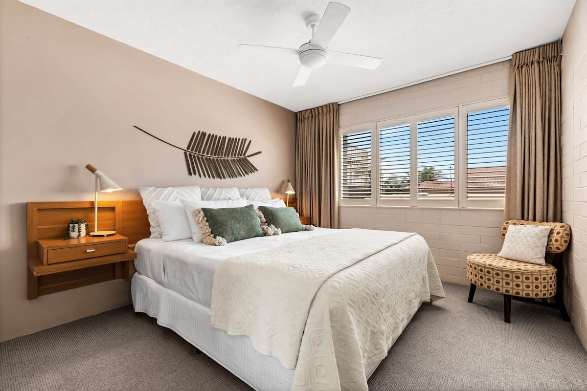 A hotel room with a bed, bedside tables, a chair, a ceiling fan, and a window with curtains.