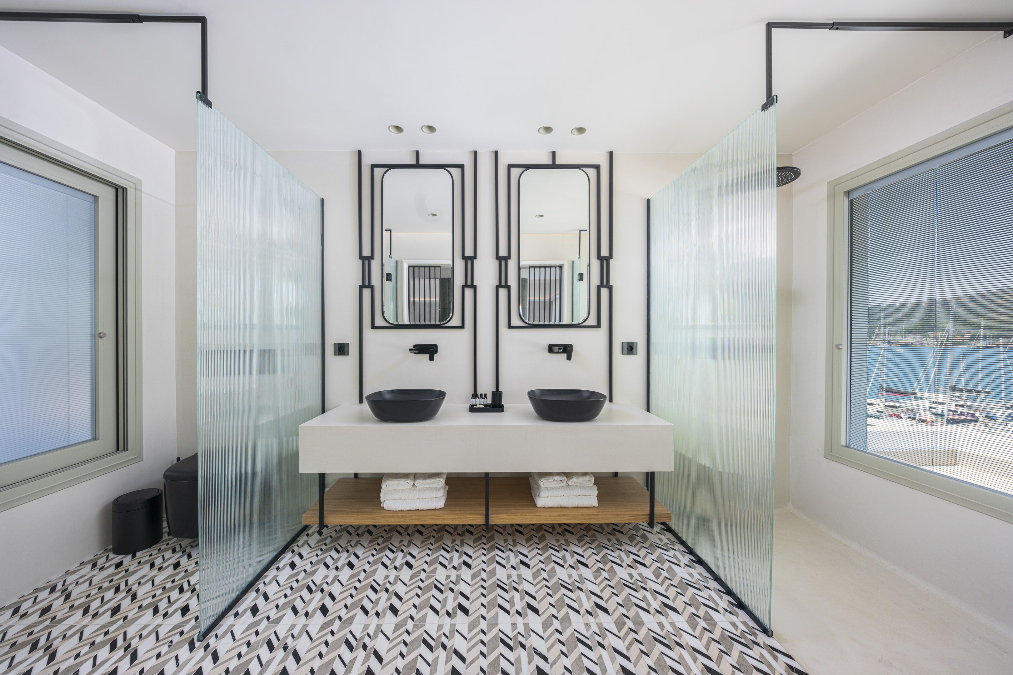 Un baño moderno con dos lavamanos, espejos grandes y un suelo estampado.