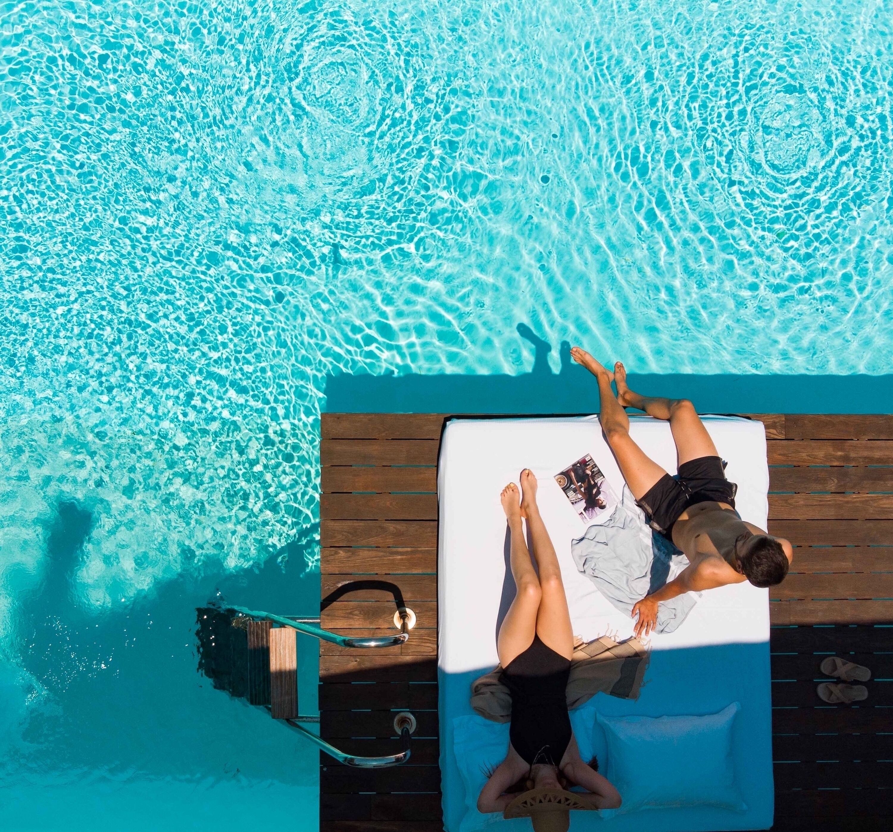 Vista aérea de una piscina con dos personas acostadas en una tumbona.