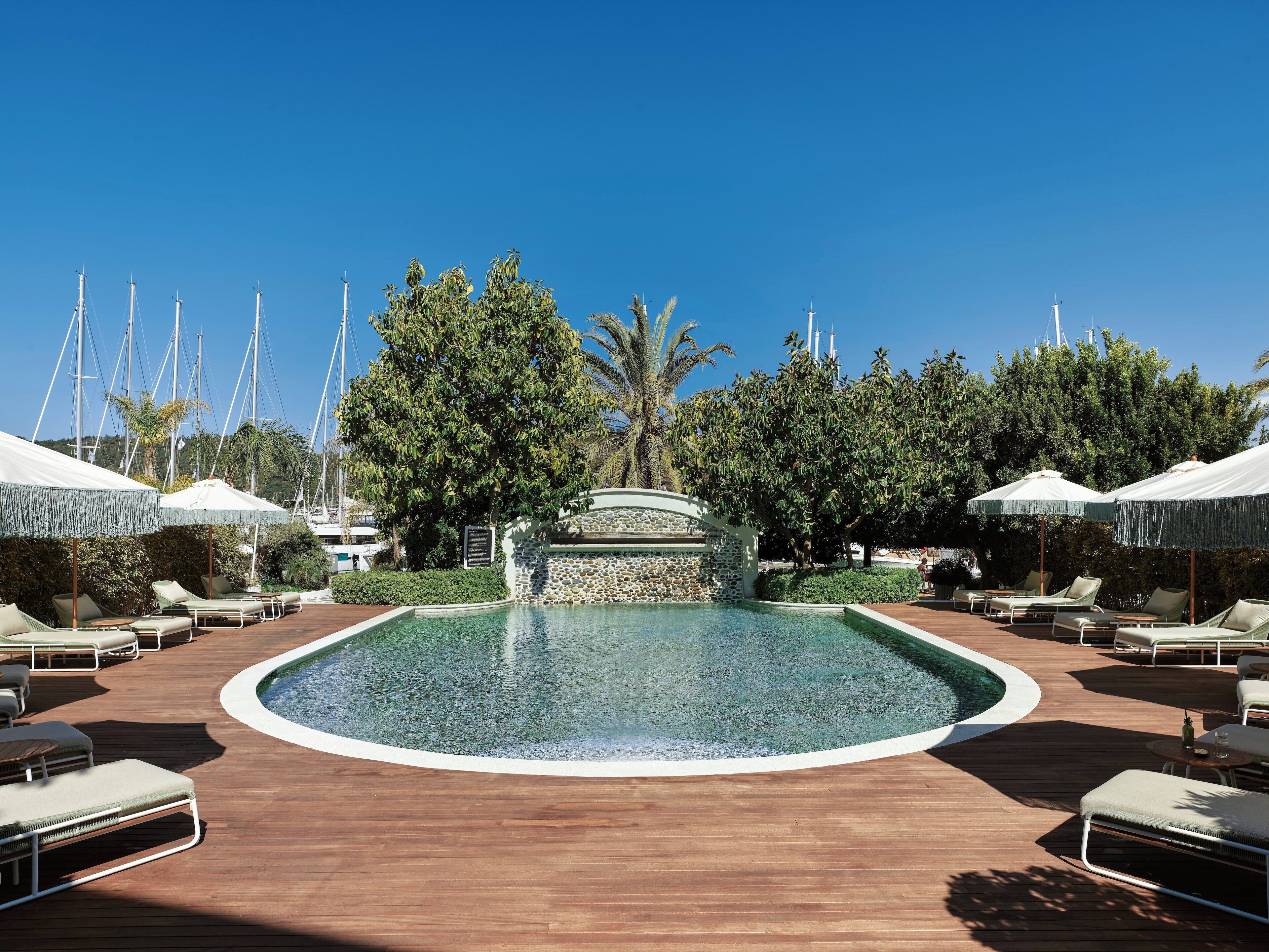 A pool area with lounge chairs and umbrellas, surrounded by trees and a stone wall.