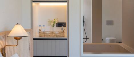 A hotel room with a bed, a bedside lamp, a small table with a vase of flowers, and a view of the bathroom.