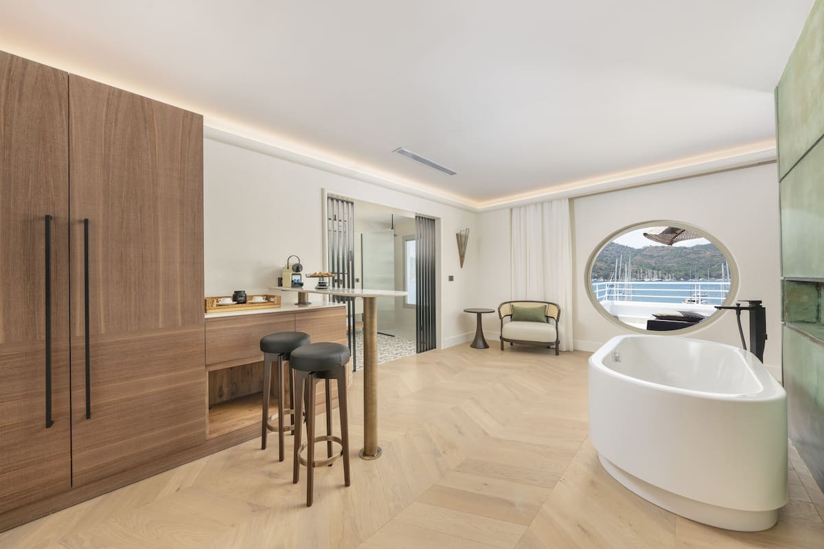A modern bathroom with a freestanding bathtub, a vanity with a mirror, and a view of the sea through a circular window.