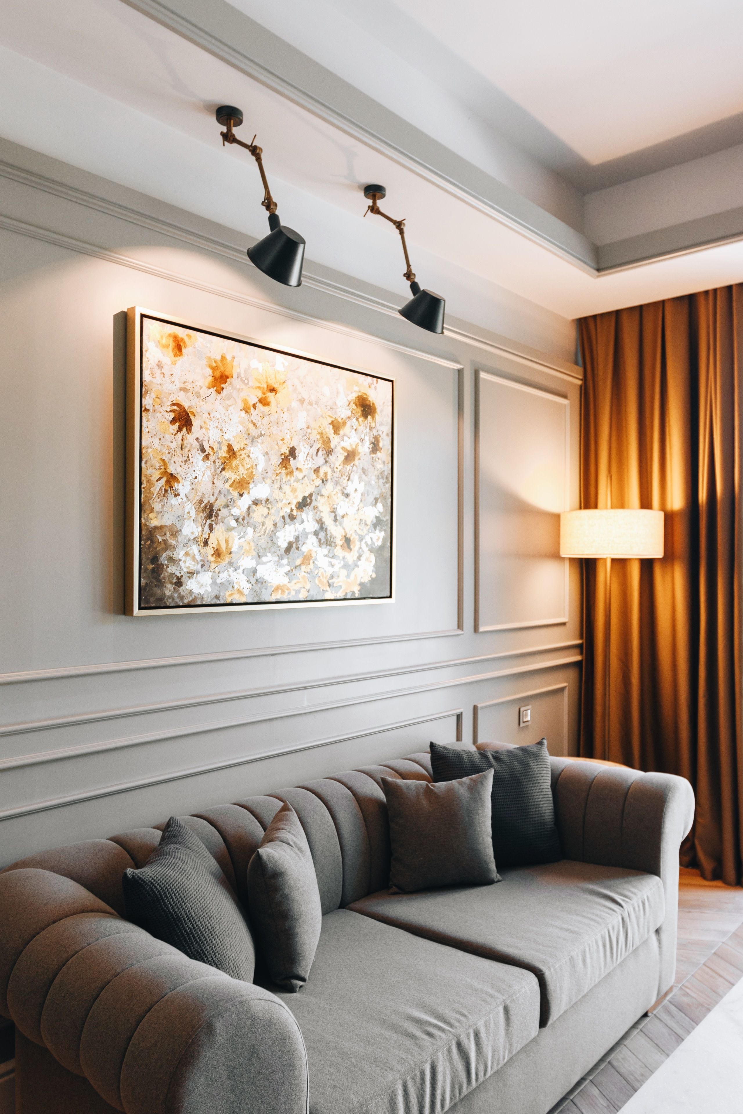 Una sala de estar moderna con un sofá gris, un cuadro abstracto grande y una lámpara de pie.