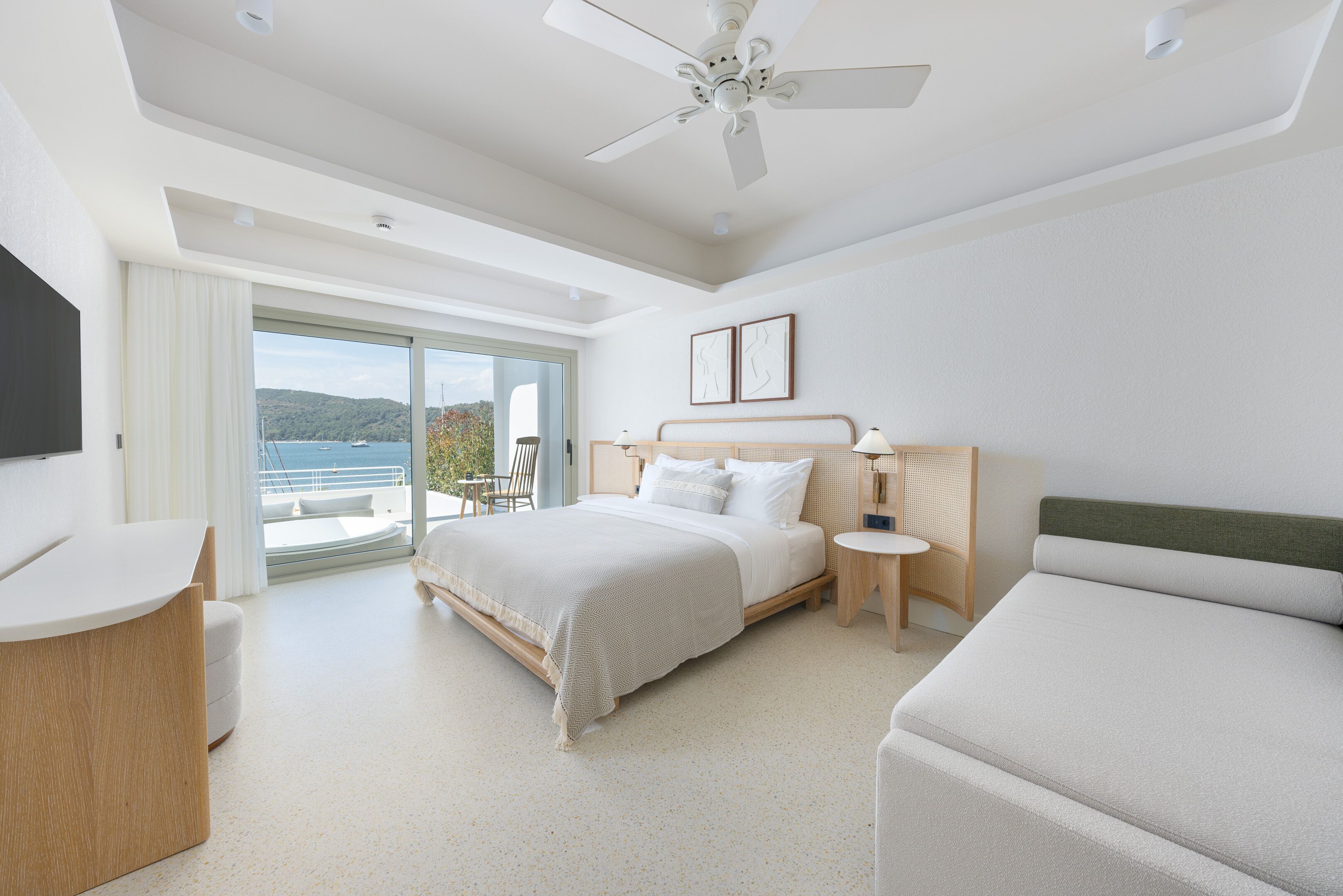 A modern hotel room with a large bed, a separate sofa, a small table, and a ceiling fan.