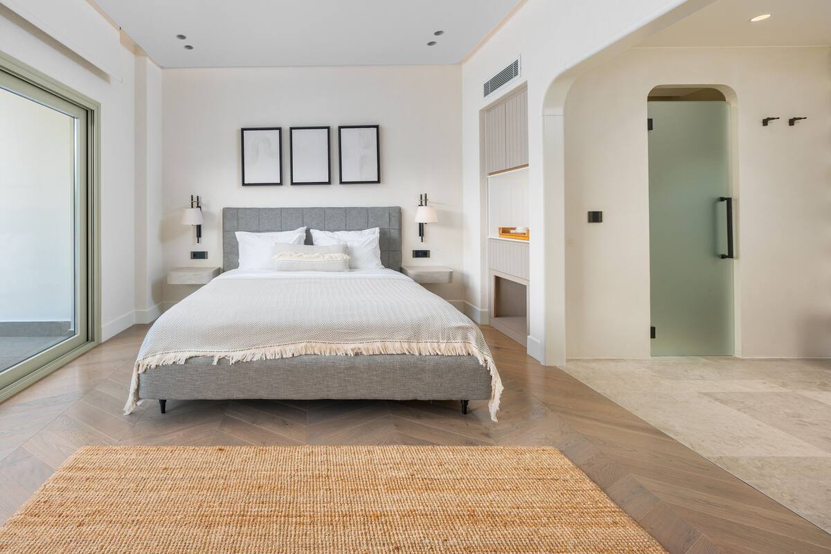 A modern bedroom with a large bed, bedside tables, and a view of the hallway.