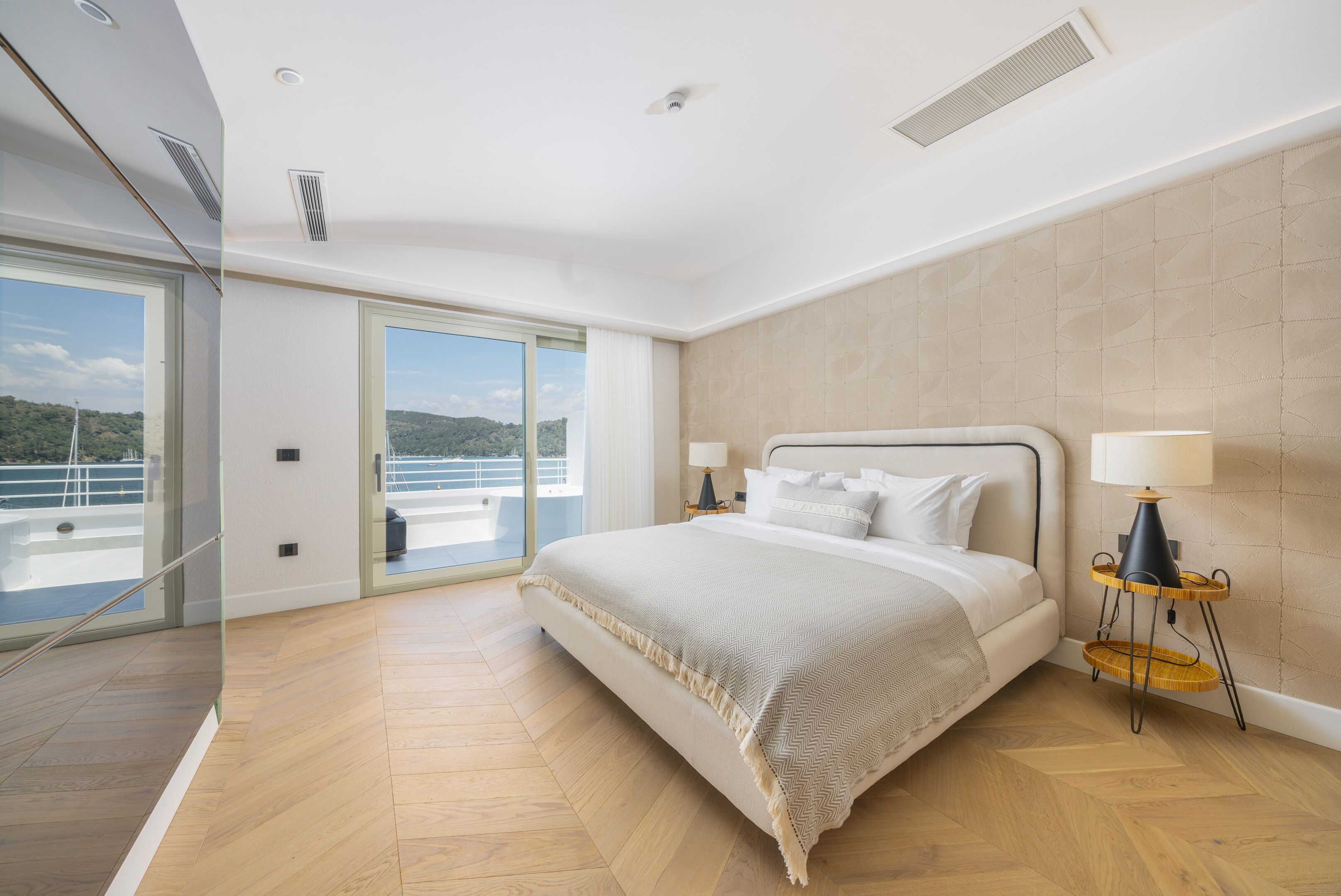 Een moderne slaapkamer met een groot bed, een glazen deur naar een balkon en uitzicht op zee.