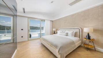 Een moderne slaapkamer met een groot bed, een glazen deur naar een balkon en uitzicht op zee.