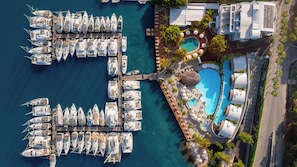 Luftaufnahme einer Marina mit zahlreichen vertäuten Booten, einem Schwimmbad und einem Gebäude mit mehreren Balkonen.