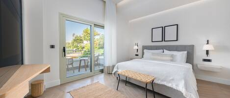 Un dormitorio moderno con una cama grande, un banco, una mesita y vistas al exterior a través de un ventanal.
