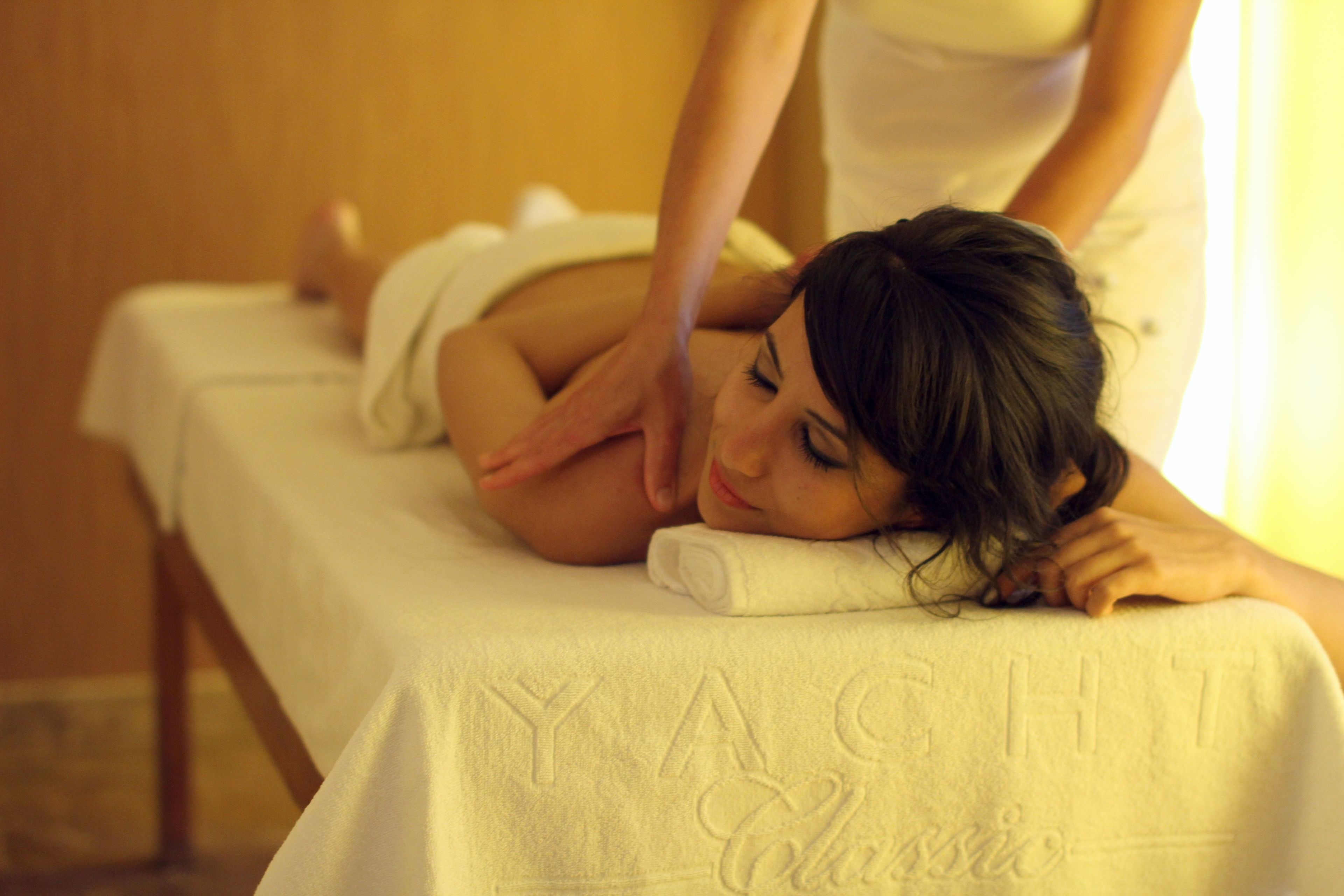 A person lying on a massage table with a towel, in a room with a wooden floor and a wall with a textured pattern.