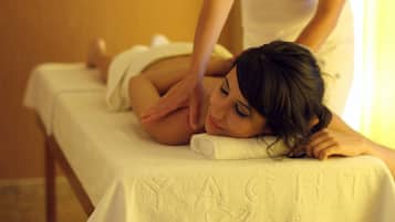 A person lying on a massage table with a towel, in a room with a wooden floor and a wall with a textured pattern.