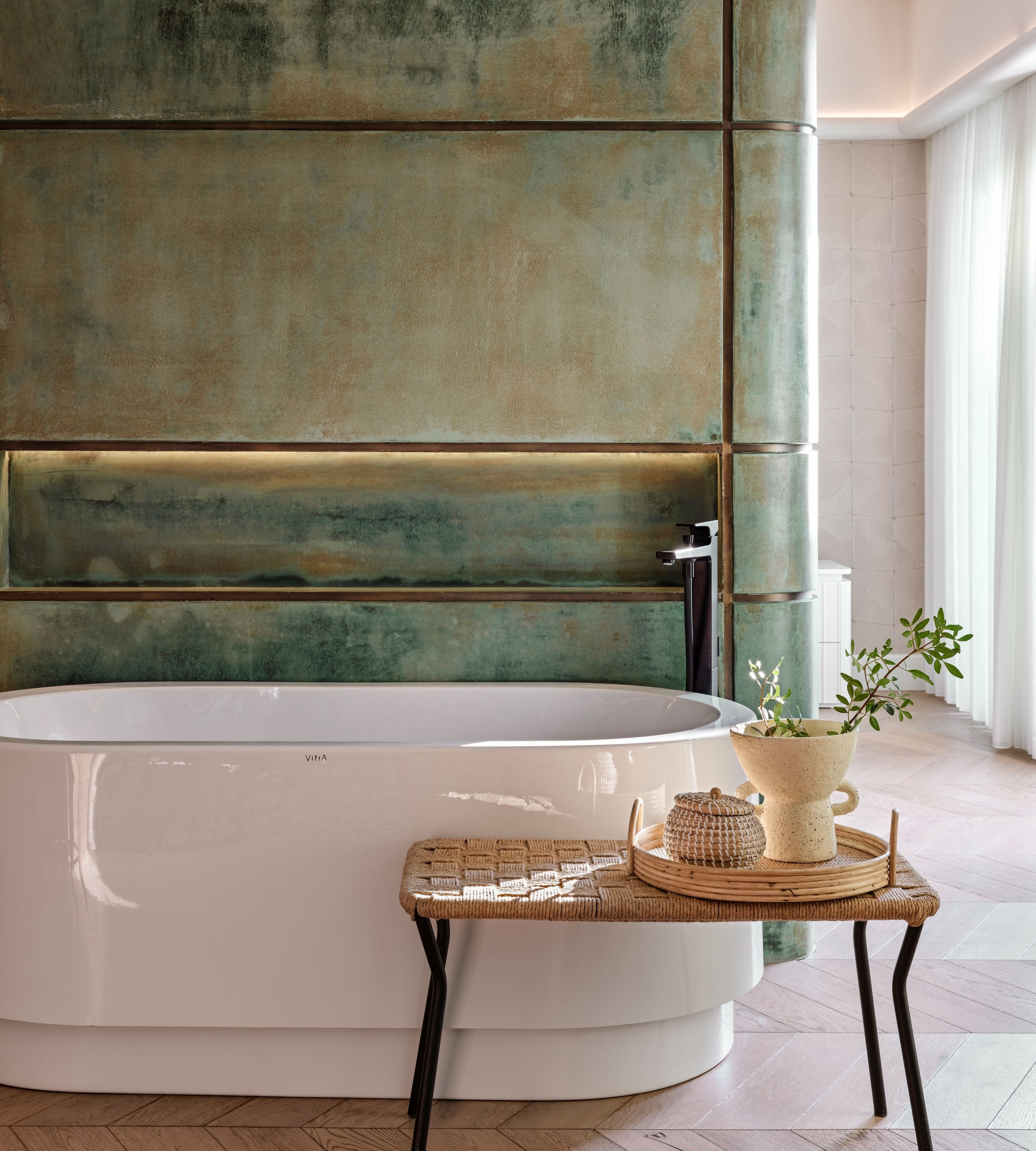 A modern bathroom with a large bathtub, a small table with a plant, and a wall with a textured finish.