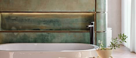 A modern bathroom with a large bathtub, a small table with a plant, and a wall with a textured finish.