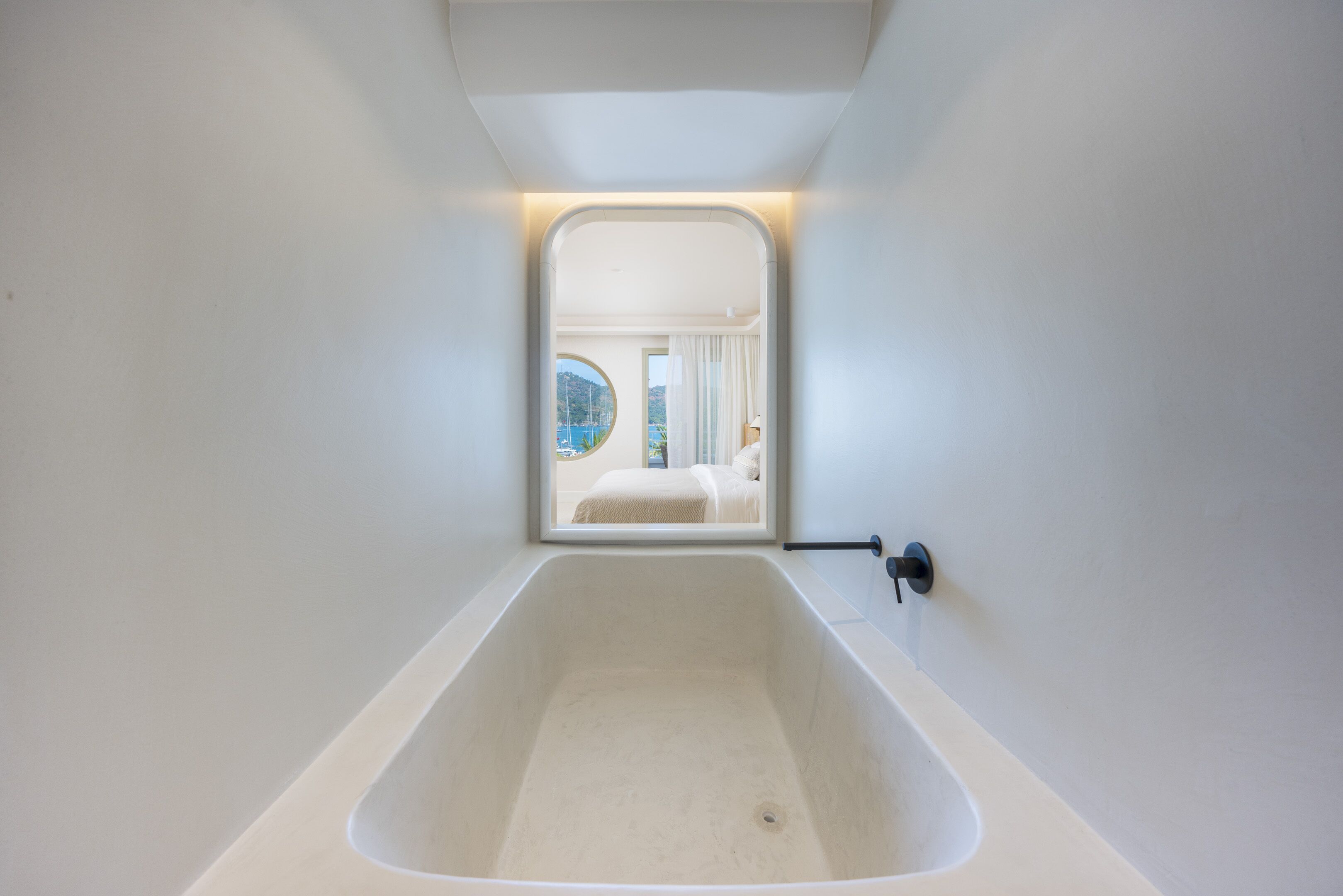 Une salle de bain moderne avec une grande baignoire, une fenêtre donnant sur une chambre et un porte-serviettes.