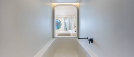 Une salle de bain moderne avec une grande baignoire, une fenêtre donnant sur une chambre et un porte-serviettes.