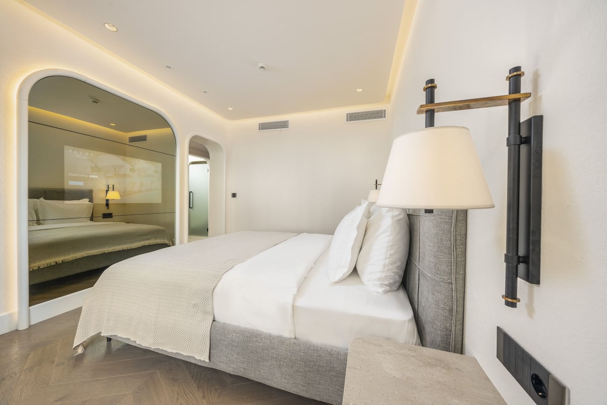 A modern bedroom with a bed, a bedside table, a lamp, and a wall-mounted shelf.
