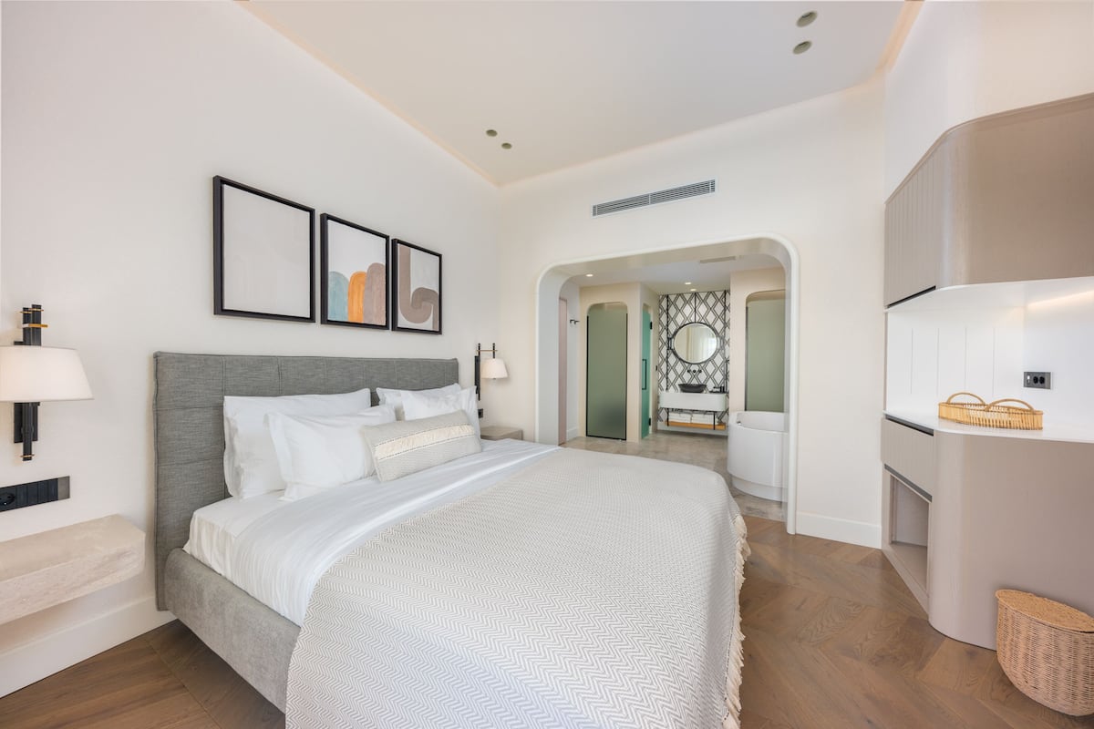 A modern hotel room with a large bed, a bedside table, a lamp, and framed artwork on the wall.