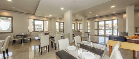 Un amplio comedor con varias mesas y sillas, ventanas grandes y vistas al exterior.