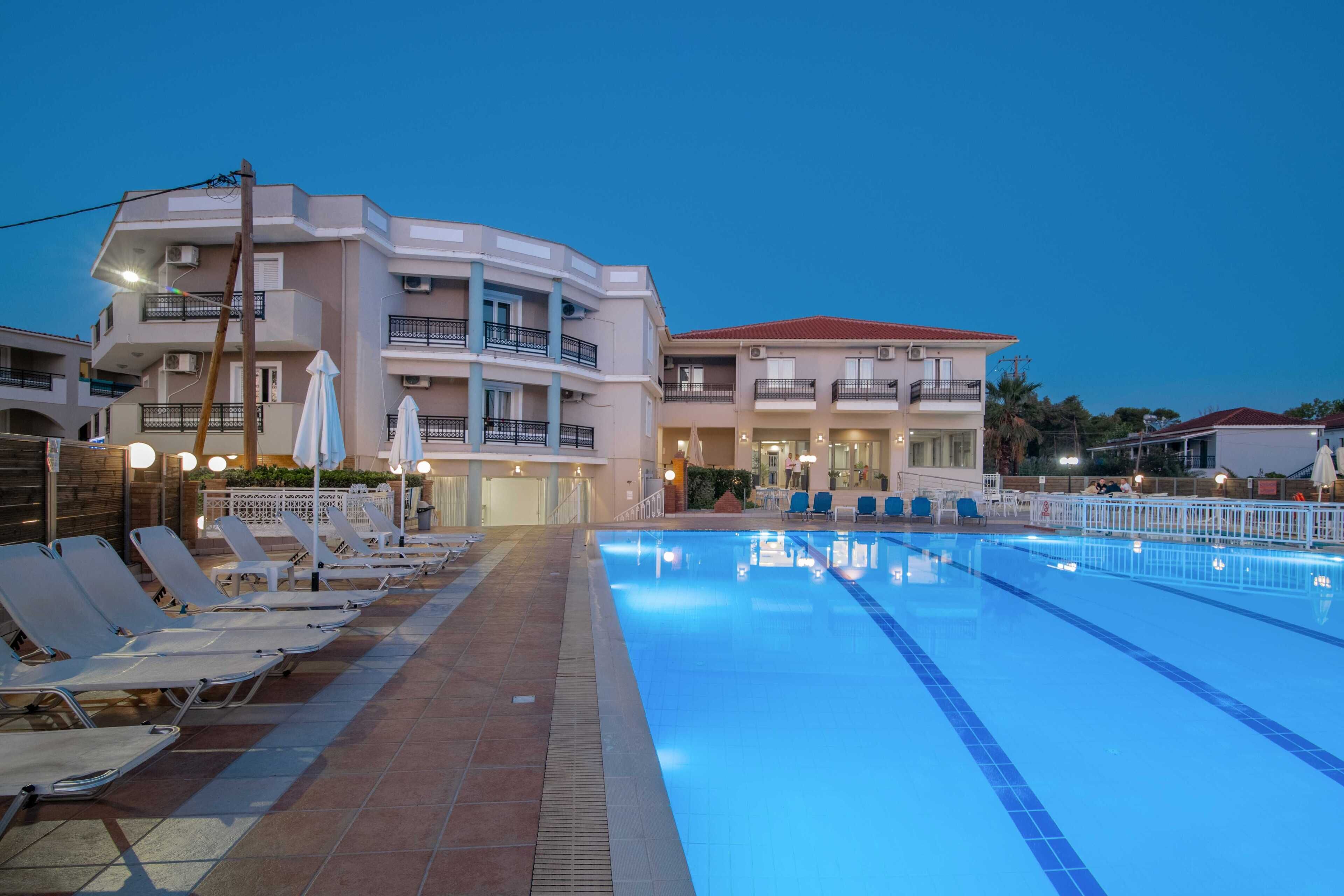 A swimming pool with lounge chairs, a building with balconies, and a clear sky.