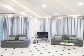 A modern living room with two grey sofas, a small coffee table, a flat-screen TV, and striped curtains.