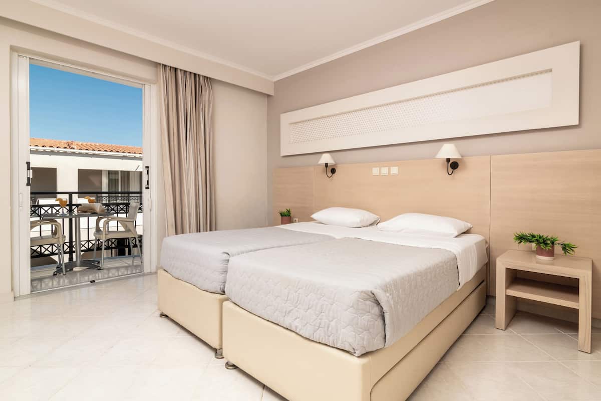 A modern bedroom with a large bed, a small bedside table, a wall-mounted light, and a view of the outside balcony.