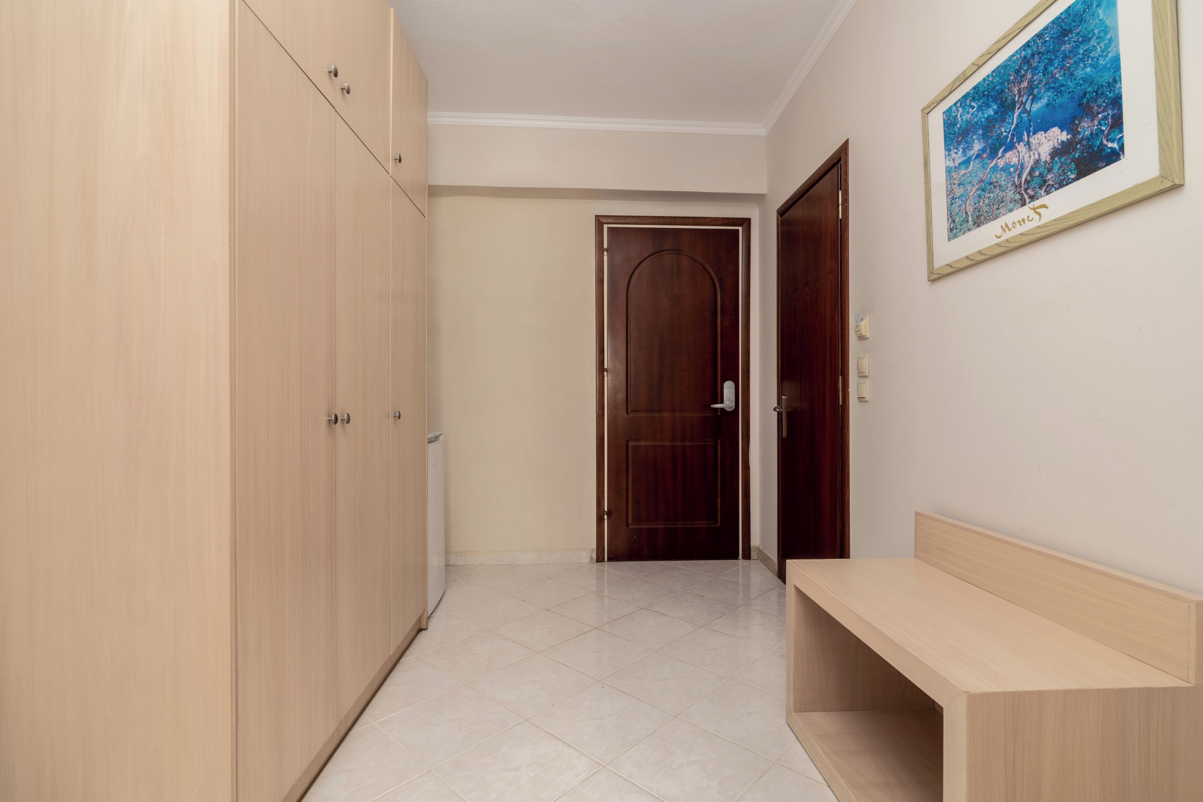 A hallway with a wooden wardrobe, a door, a bench, and a framed picture on the wall.