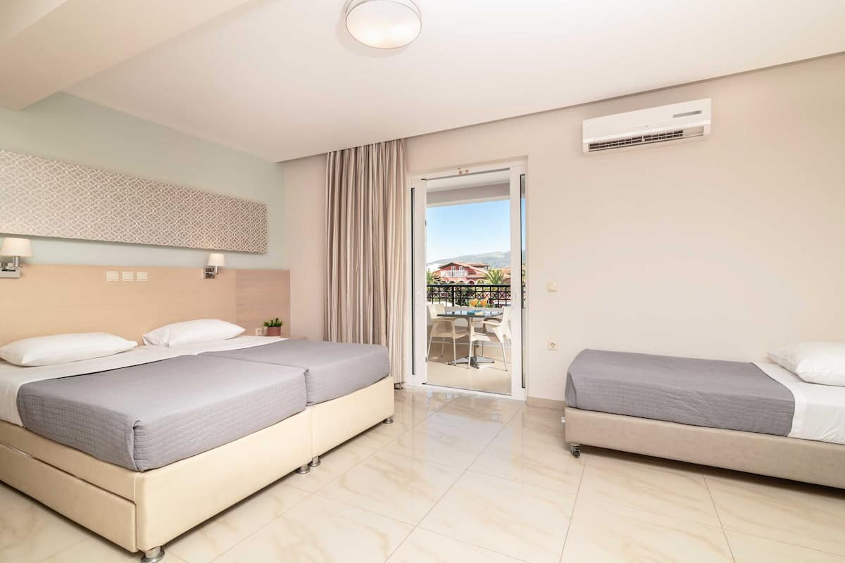 A hotel room with two beds, a balcony with a view, and an air conditioning unit on the wall.