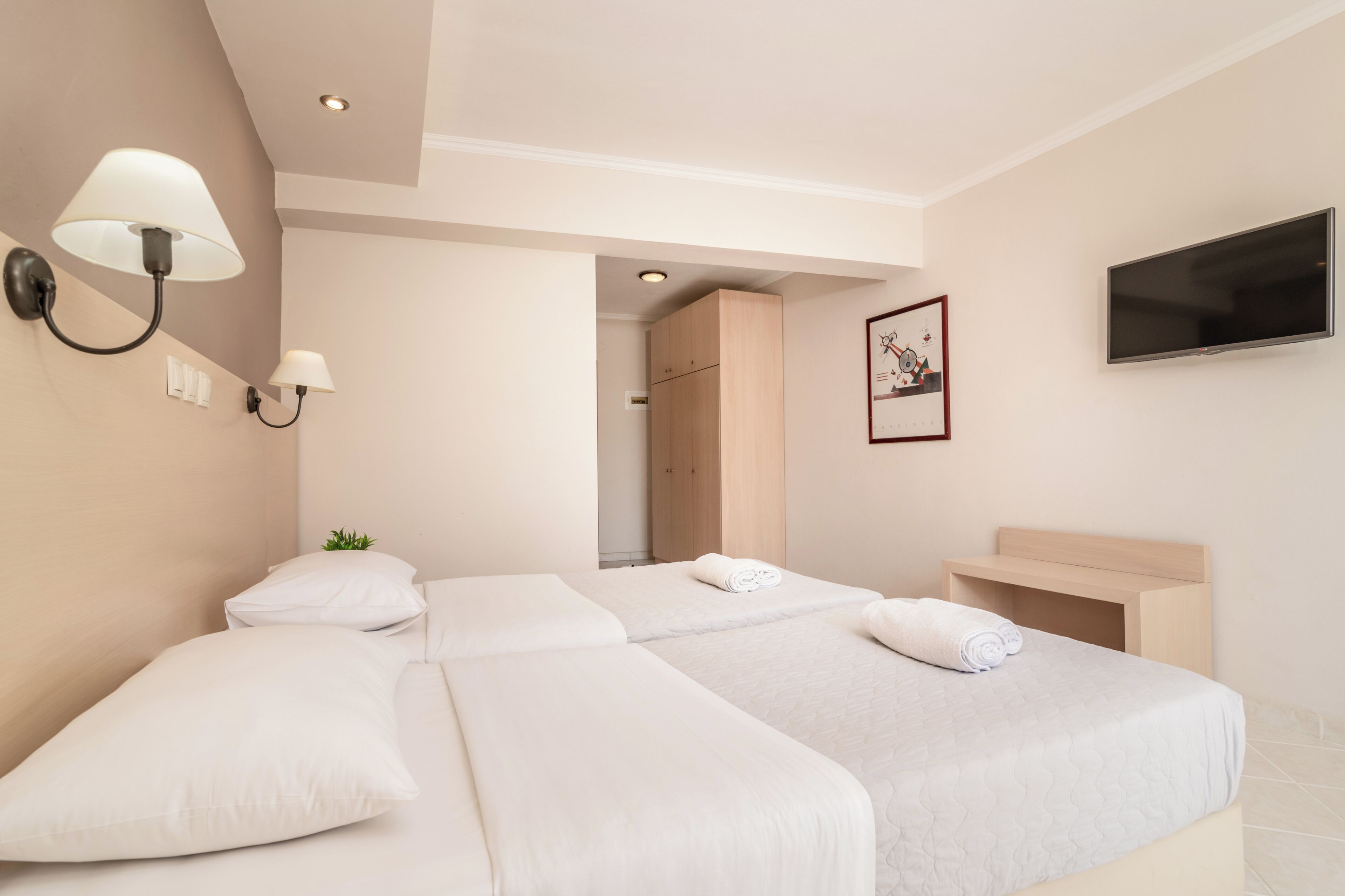 A hotel room with two beds, a TV, a painting, and a bathroom visible through an open door.