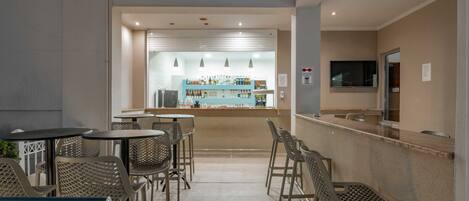 A bar area with metal chairs and tables, a counter with a TV, and a view of the bar area in the background.