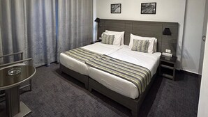 Una habitación de hotel moderna con una cama grande, una mesita de noche con lámpara, un escritorio pequeño y una silla.