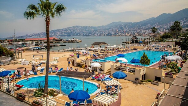 Un resort con varias piscinas, tumbonas y vistas a la ciudad y las montañas.
